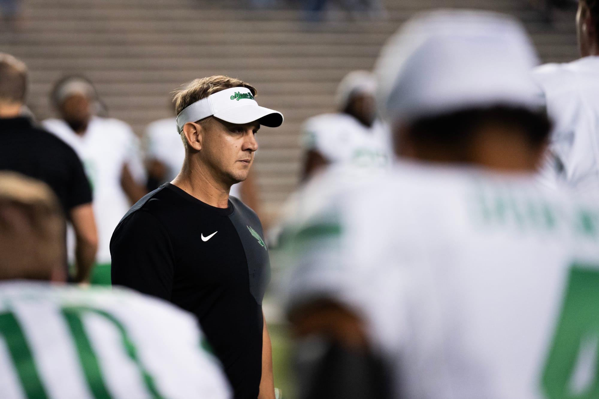 Eric Morris watches from sideline in North Texas visor and black Nike shirt during Mean Green's 2025 season before becoming Oklahoma State head coach