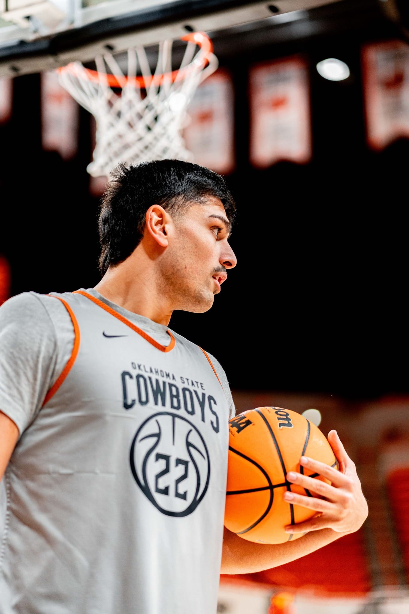 Oklahoma State center Parsa Fallah (22) holds a basketball during warmups at Gallagher-Iba Arena with the basket and championship banners visible in the background.