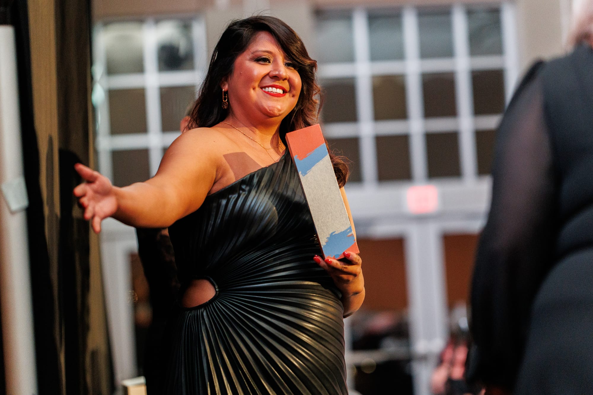 Mandy Lyons smiles and gestures while holding a Chamber award trophy as she prepares to present the Volunteer of the Year Award at the Stillwater Chamber Awards Gala.