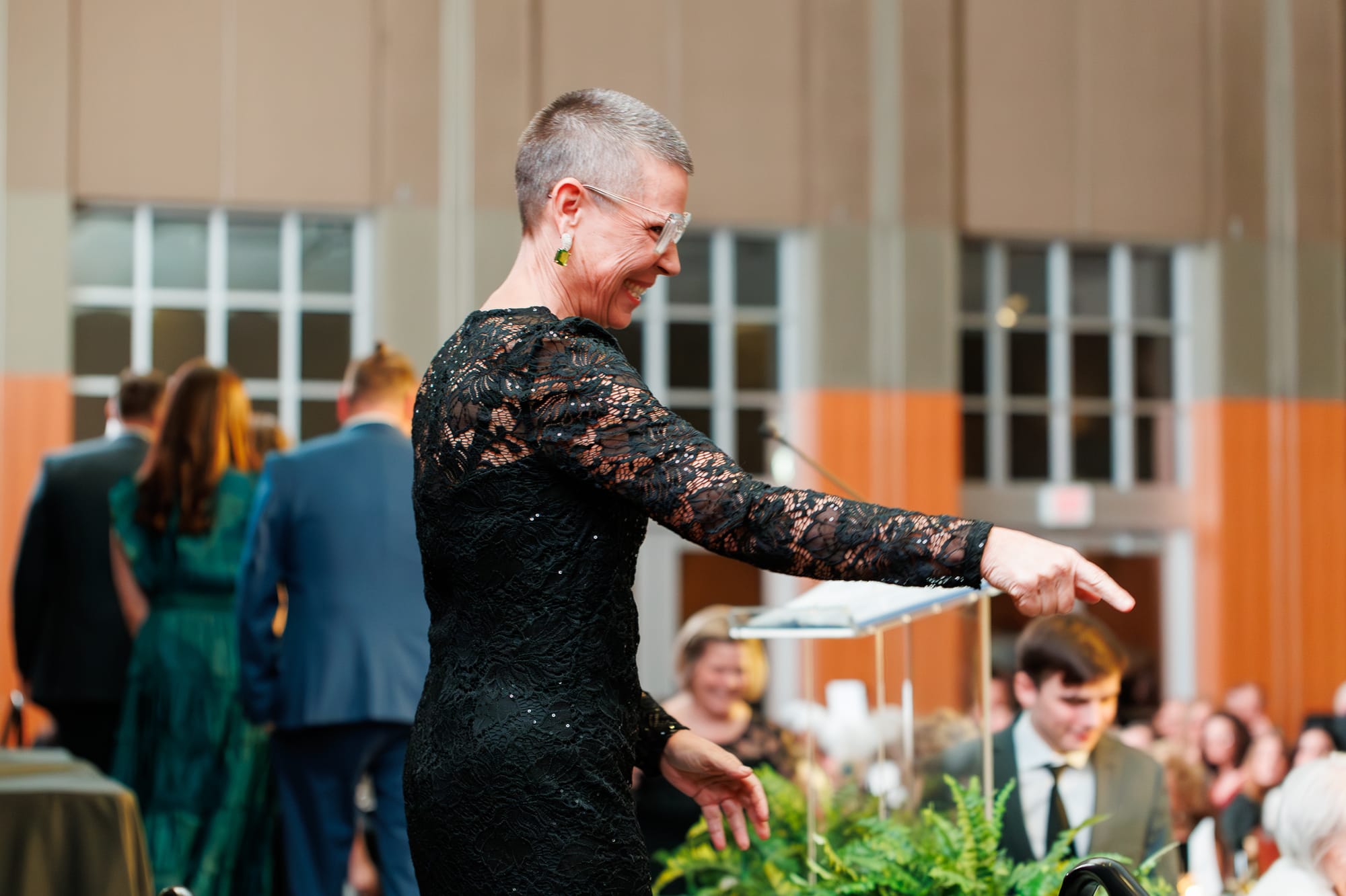 Alane Zannotti smiles and points toward the audience from the stage during the Stillwater Chamber of Commerce Awards Gala, with a seated crowd visible in the background.