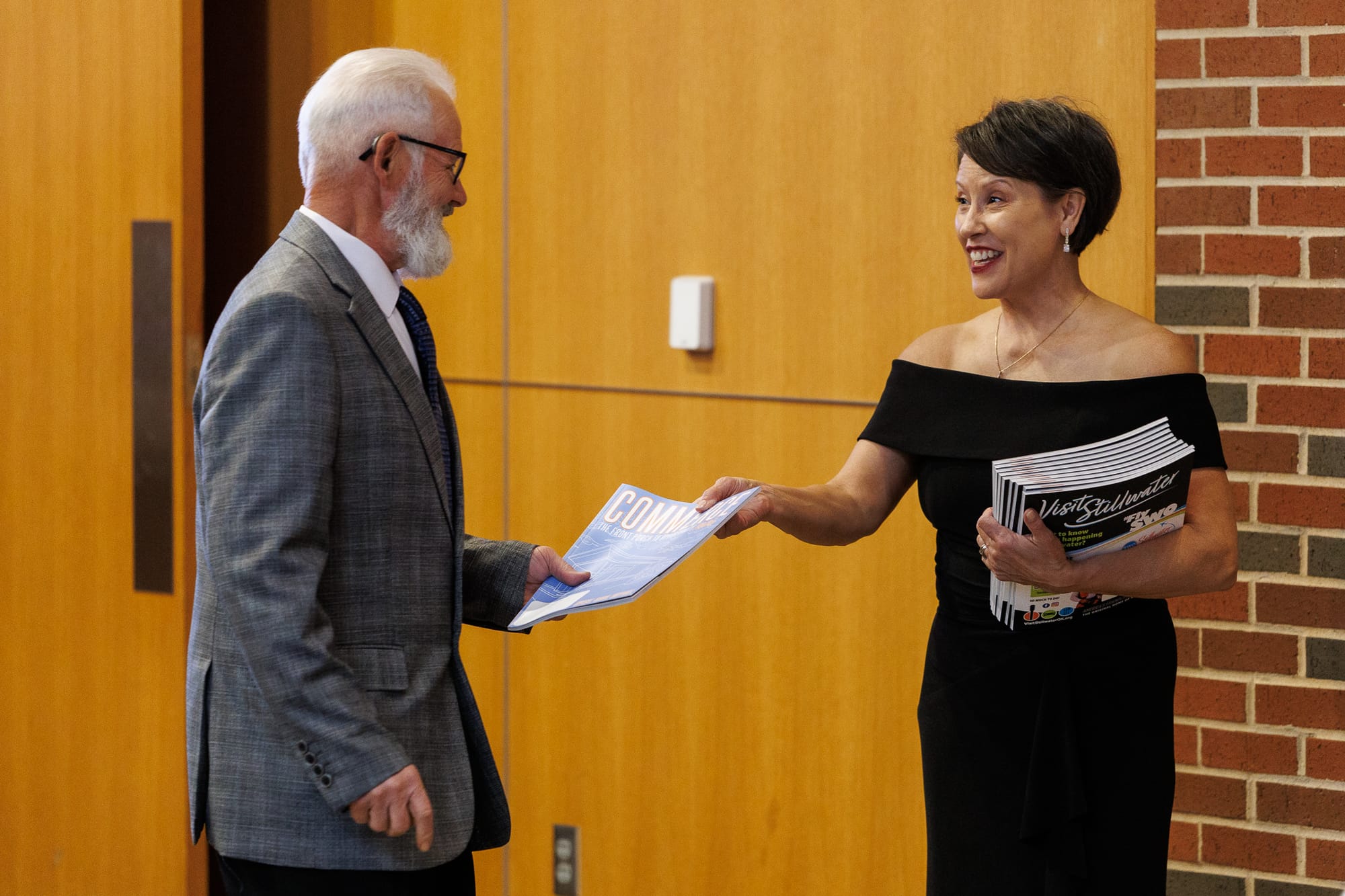 Kimie Calcagno smiles as she hands a copy of the Chamber's Commerce Magazine to a guest while holding a stack of publications at the Stillwater Chamber Awards Gala.