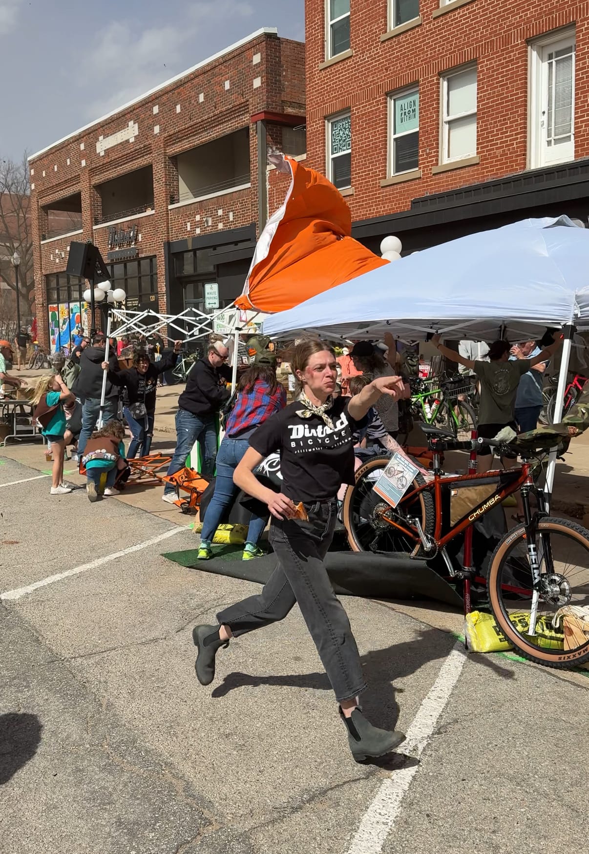 Crystal Wintle in a District Bicycles shirt runs across West 7th Avenue as high winds send an orange tent cover flying behind her during the 2025 Mid South expo.