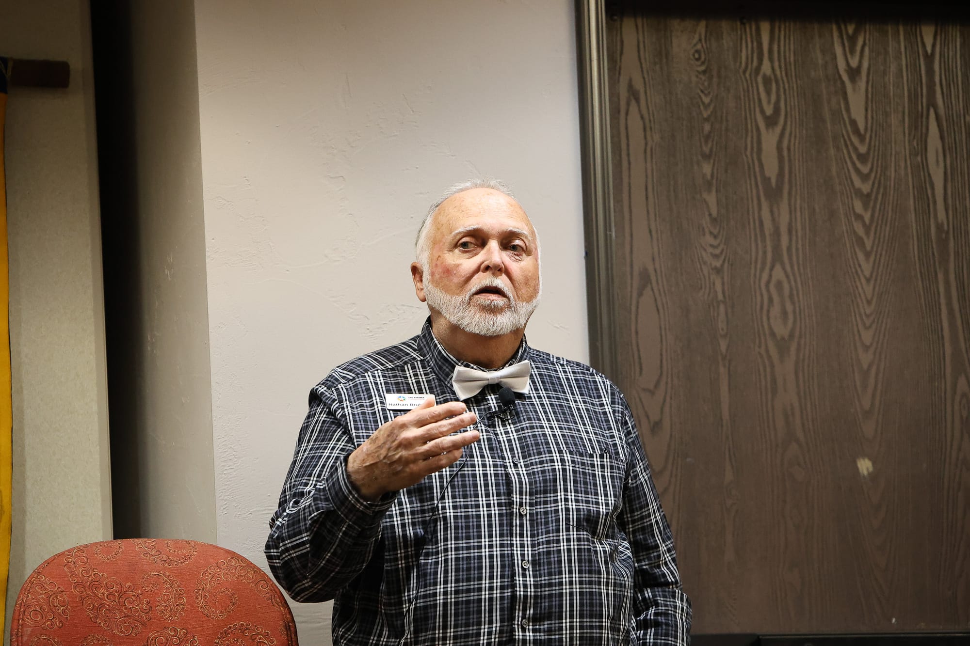 Nathan Brubaker, an older man with white hair and a bow tie, gestures while speaking at the Stillwater Frontier Rotary Club candidate forum on March 19.