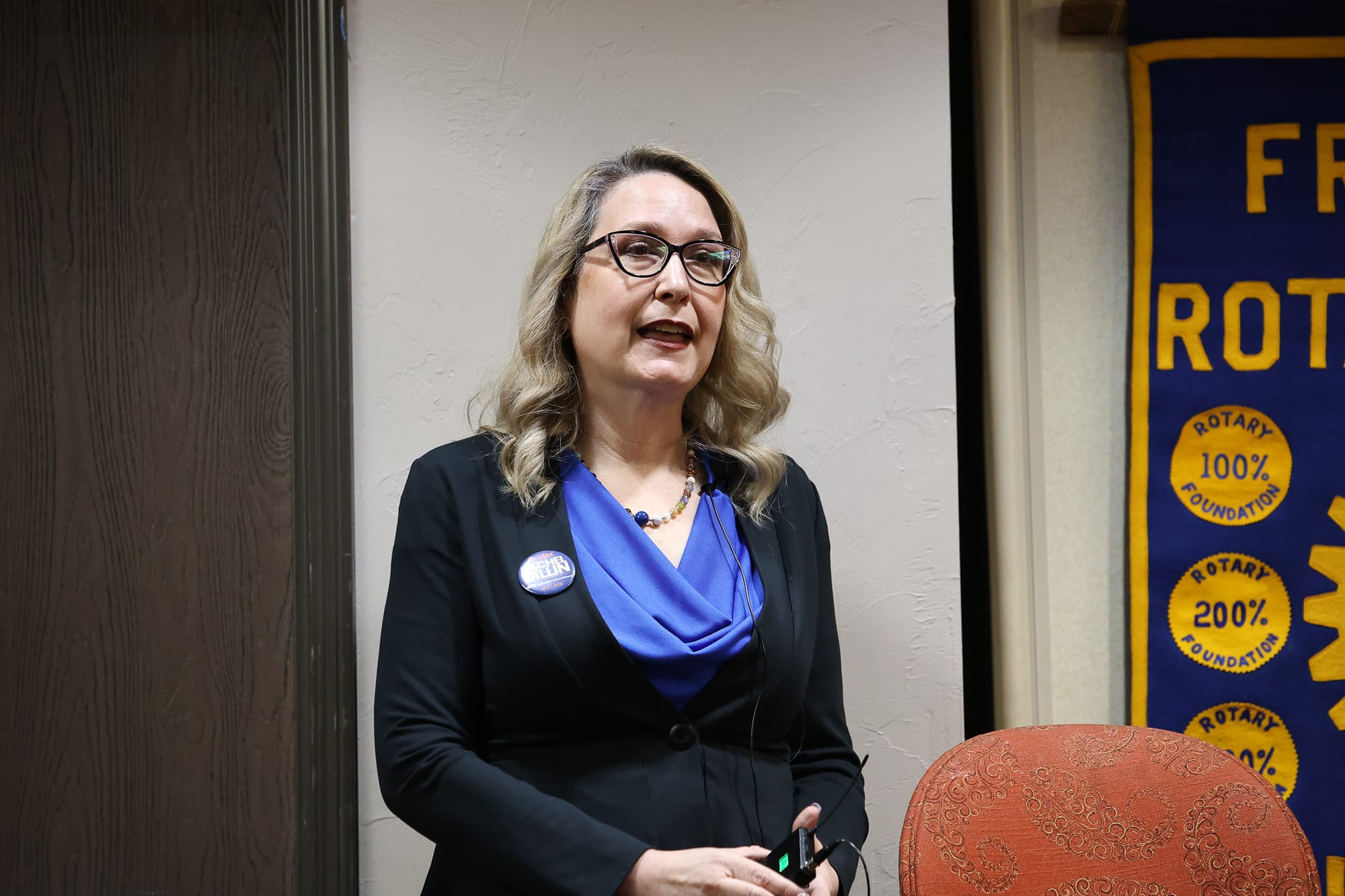 Rachel Dillin, a woman with blonde hair and black-rimmed glasses, speaks at the March 19 Stillwater Frontier Rotary Club candidate forum. She wears a black blazer and blue top.