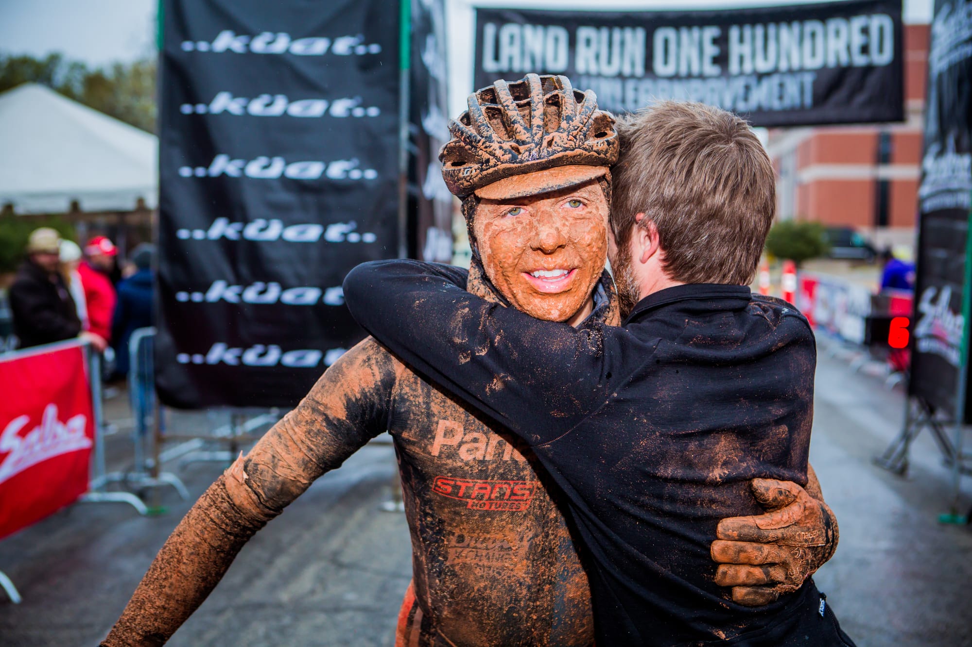 Rob Bell, caked in mud, smiles while embracing Bobby Wintle at the 2017 Land Run 100 finish line after winning the rain-soaked race. Only 165 of 850 starters finished.