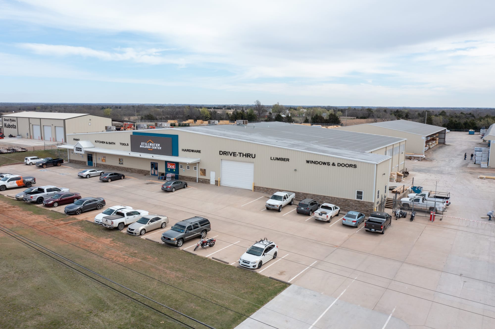 Aerial view of the Stillwater Building Center store and parking lot at 44th and Perkins Road, with signage for lumber, windows and doors, hardware, and drive-thru visible on the building exterior.