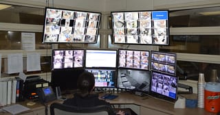 A detention center employee sitting at a desk with ten monitors showing cameras in the jail