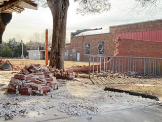 A pile of bricks from volunteers who demolished a wall. The original building with broken windows can be seen.