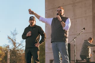 Trenton Inselman and Mayor Will Joyce hold cans of Shimai Toshi beer on stage at Stillwater Harvest Festival, with Joyce raising his can in the air
