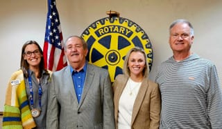 Four people standing in front of Rotary Club emblem and American flag. From left: Rachael Condley, Mike Woods, Abbey Davis and Chris Norris at Stillwater Frontier Rotary.