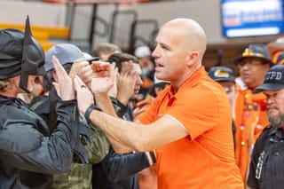 Oklahoma State head coach Steve Lutz in an orange polo high-fives fans in the student section at Gallagher-Iba Arena, including one fan wearing a Batman costume.