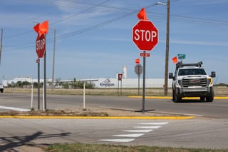Newly installed all-way stop signs with orange warning flags at the intersection of East Airport Road and North Perkins Road, with the Kingspan facility visible in the background.