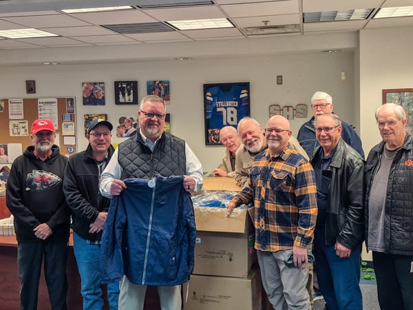 Stillwater High School Principal Walter Howell holds a blue winter coat while standing with Knights of Columbus Council 5266 members in his office