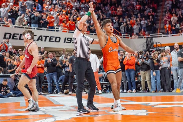 Oklahoma State wrestler Alex Facundo in orange singlet has hand raised in victory by referee after defeating Oklahoma opponent on Jan. 11, 2026, at Gallagher-Iba Arena.