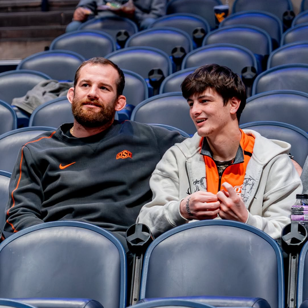OSU wrestling coach David Taylor sits with top recruit Jax Forrest. Taylor wears OSU Nike gear while Forrest wears an orange pullover and grey hoodie.