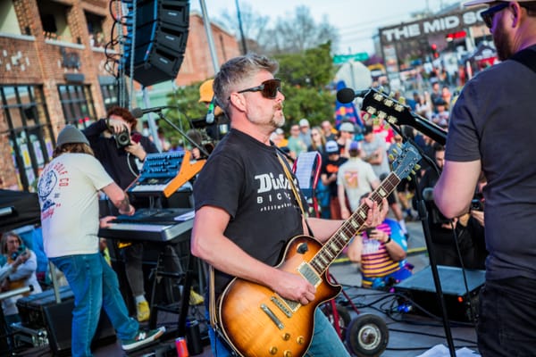 Bobby Wintle plays a sunburst Les Paul guitar at a microphone on an outdoor stage during The Mid South 2024, with a keyboard player behind him, a packed crowd.